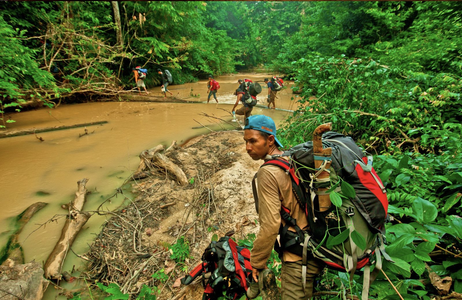 The expedition team wading up a muddy jungle river to reach Liang Tebo
